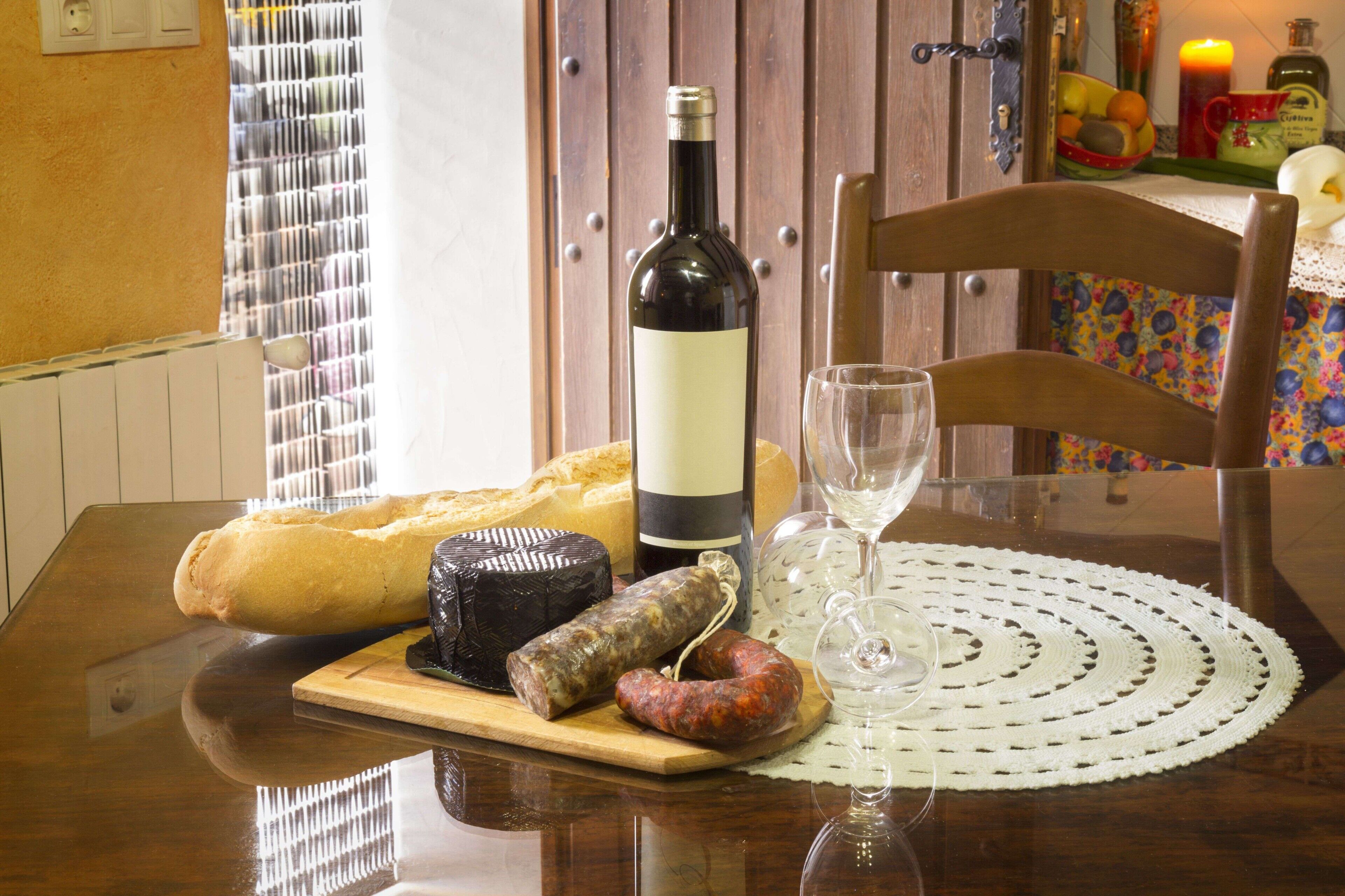Een eettafel met een fles wijn, een glas, een brood en verschillende soorten vleeswaren.