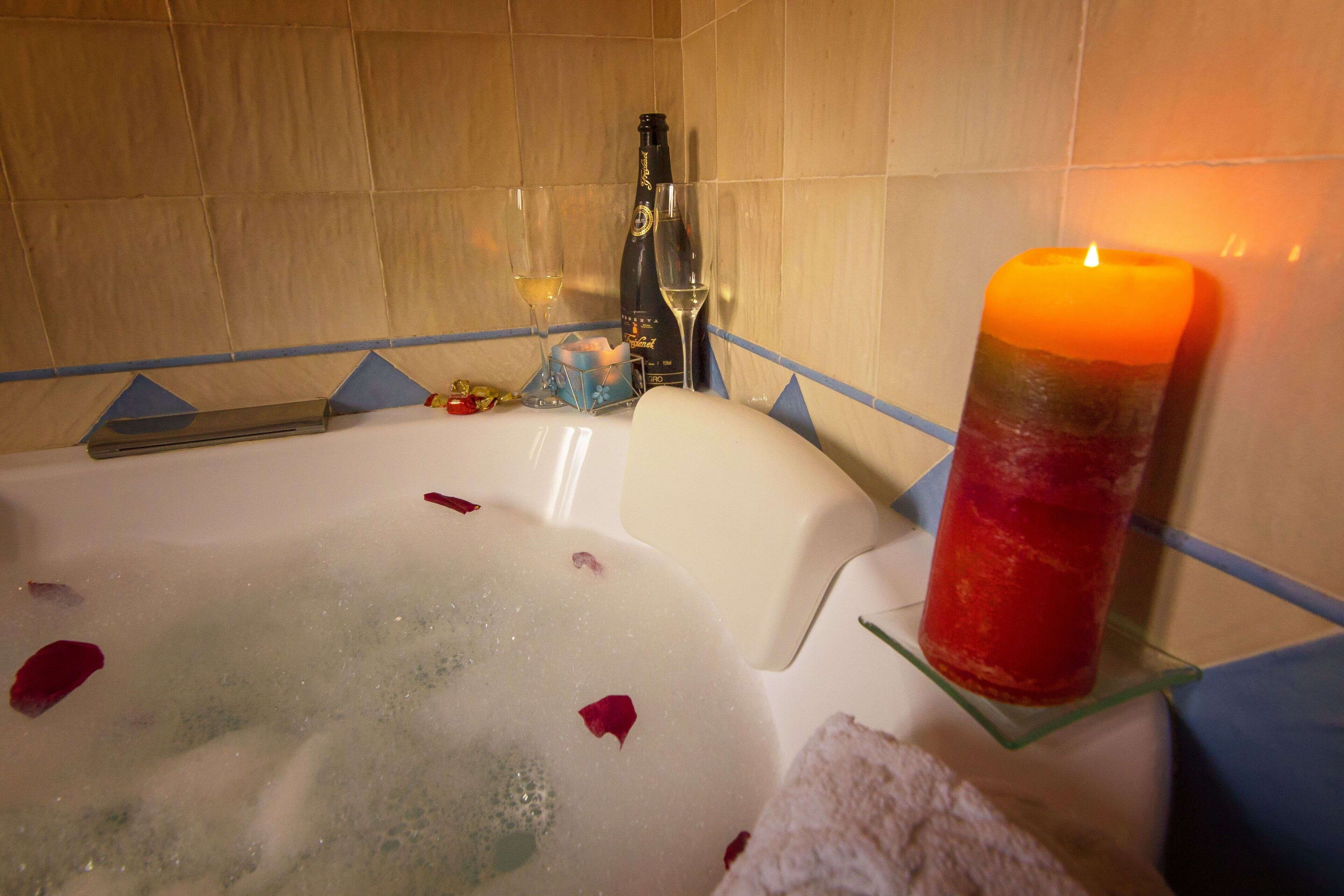 Une baignoire remplie de pétales de rose, une bougie et une bouteille de champagne.