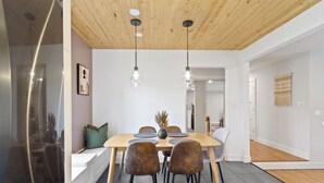 Ein moderner Essbereich mit Holzbalkendecke, einem großen Tisch mit Stühlen und Pendelleuchten.