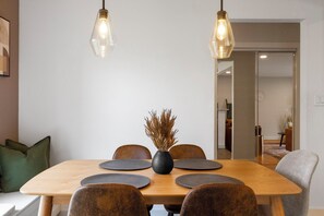 Un coin repas comprenant une table en bois, six chaises, un vase contenant des plantes séchées et deux lampes suspendues.
