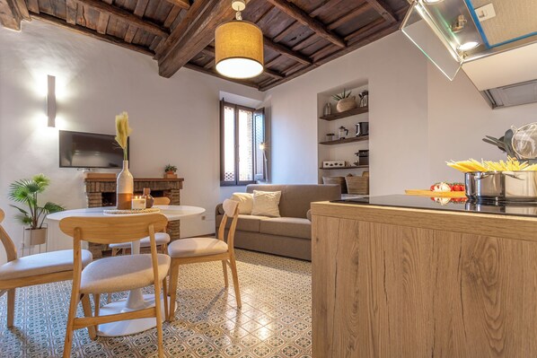 A cozy living area with a wooden ceiling, a dining table with chairs, a sofa, and a kitchen counter with a sink and utensils. - 18 Ciancaleoni House (Roma)