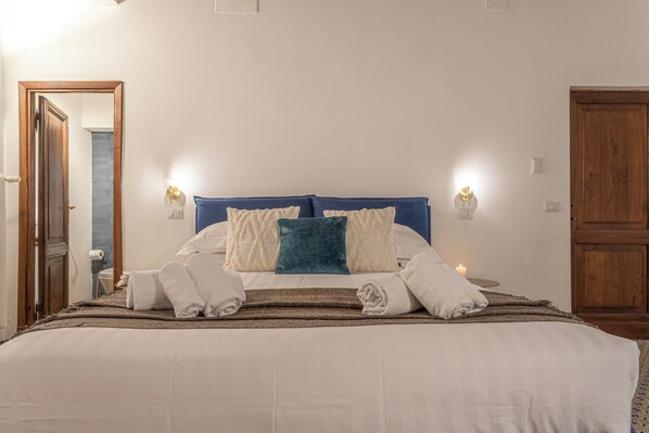 A neatly made bed with white and blue bedding, two wall-mounted lights, and a bedside table with a candle. - 18 Ciancaleoni House (Roma)