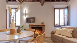 Een gezellige woonkamer met een open haard, een bank, een aan de muur bevestigde televisie en een eettafel met stoelen.