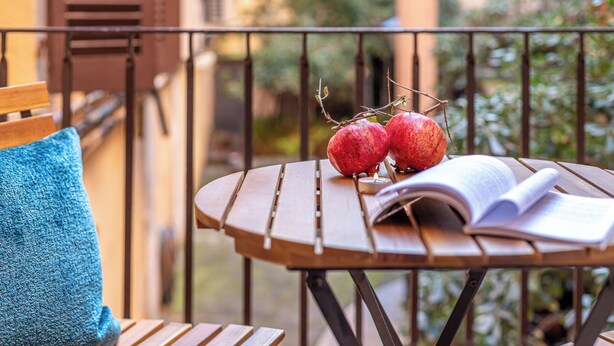 Een houten tafel met twee appels en een open boek op een balkon.