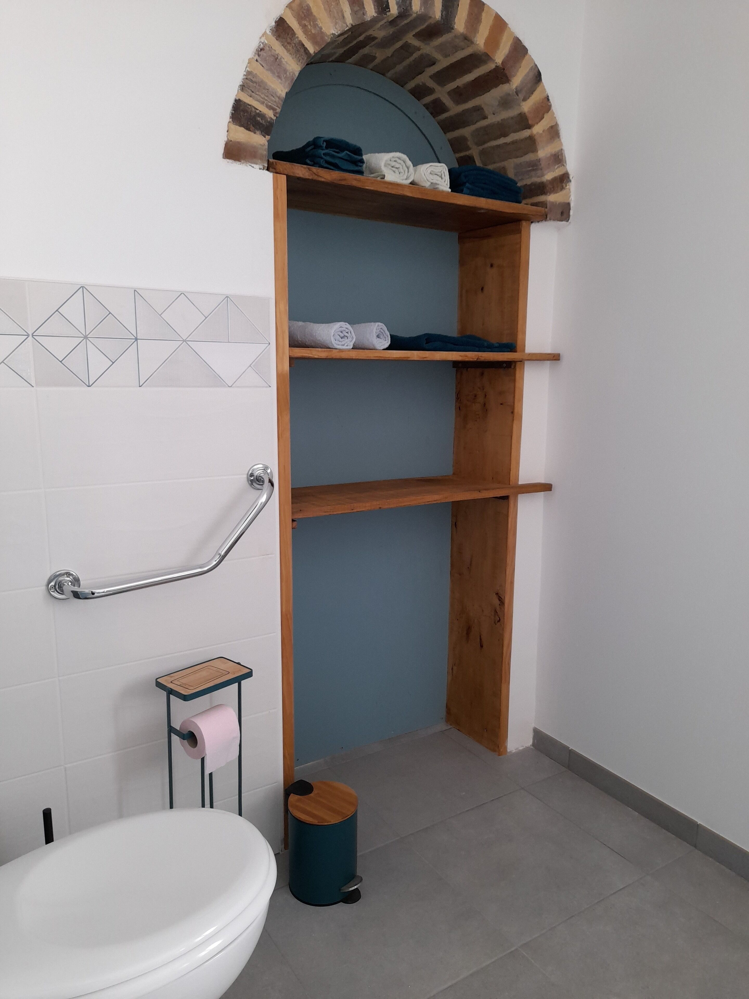 Ein Badezimmer mit Toilette, einer Holzanrichte mit Handtüchern, einer Handstange und einer kleinen Mülltonne.