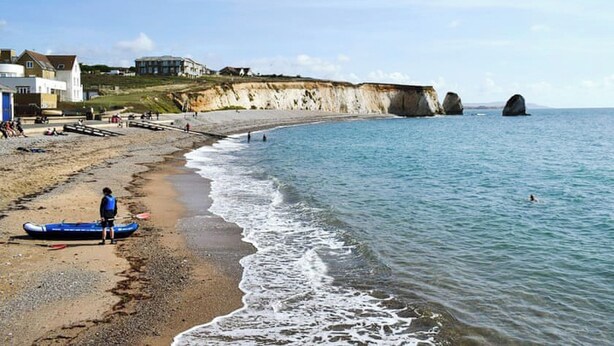 A beach with a rocky cliff, a building, and a person in a kayak. - 4 bedroom accommodation in Freshwater (Freshwater)