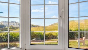 A room with a large window offering a view of a building and a grassy landscape. - 4 bedroom accommodation in Freshwater (Freshwater)