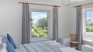 A bedroom with a large window, a bed with striped bedding, a chair, and a bedside table. - 4 bedroom accommodation in Freshwater (Freshwater)