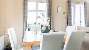 Ein Zimmer mit einem Esstisch, Stühlen, einer Topfpflanze, einer Weinflasche und Blick ins Freie.