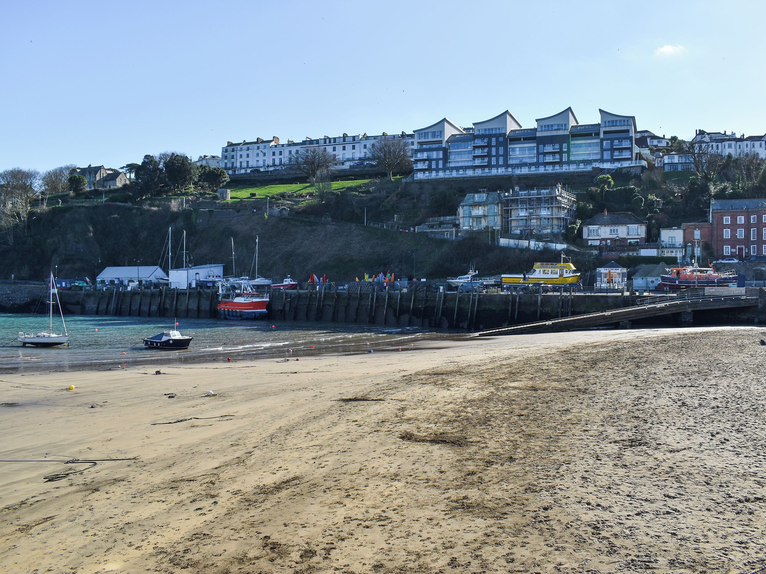 A coastal area with a sandy beach, boats, and buildings in the background.
