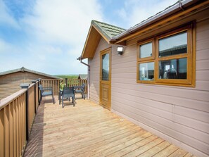 Une terrasse en bois avec des chaises et une table, une porte en bois et des fenêtres donnant sur le paysage.