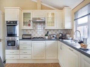 A modern kitchen with white cabinets, a built-in oven, a toaster, a kettle, and a sink.