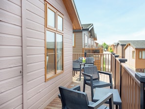 A wooden deck with outdoor furniture, a railing, and a view of adjacent cabins.