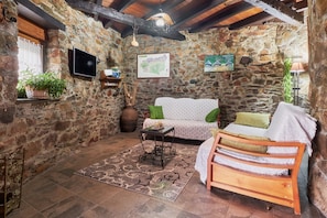 A stone-walled room with a sofa, a wooden bench, a small table, and a map on the wall.