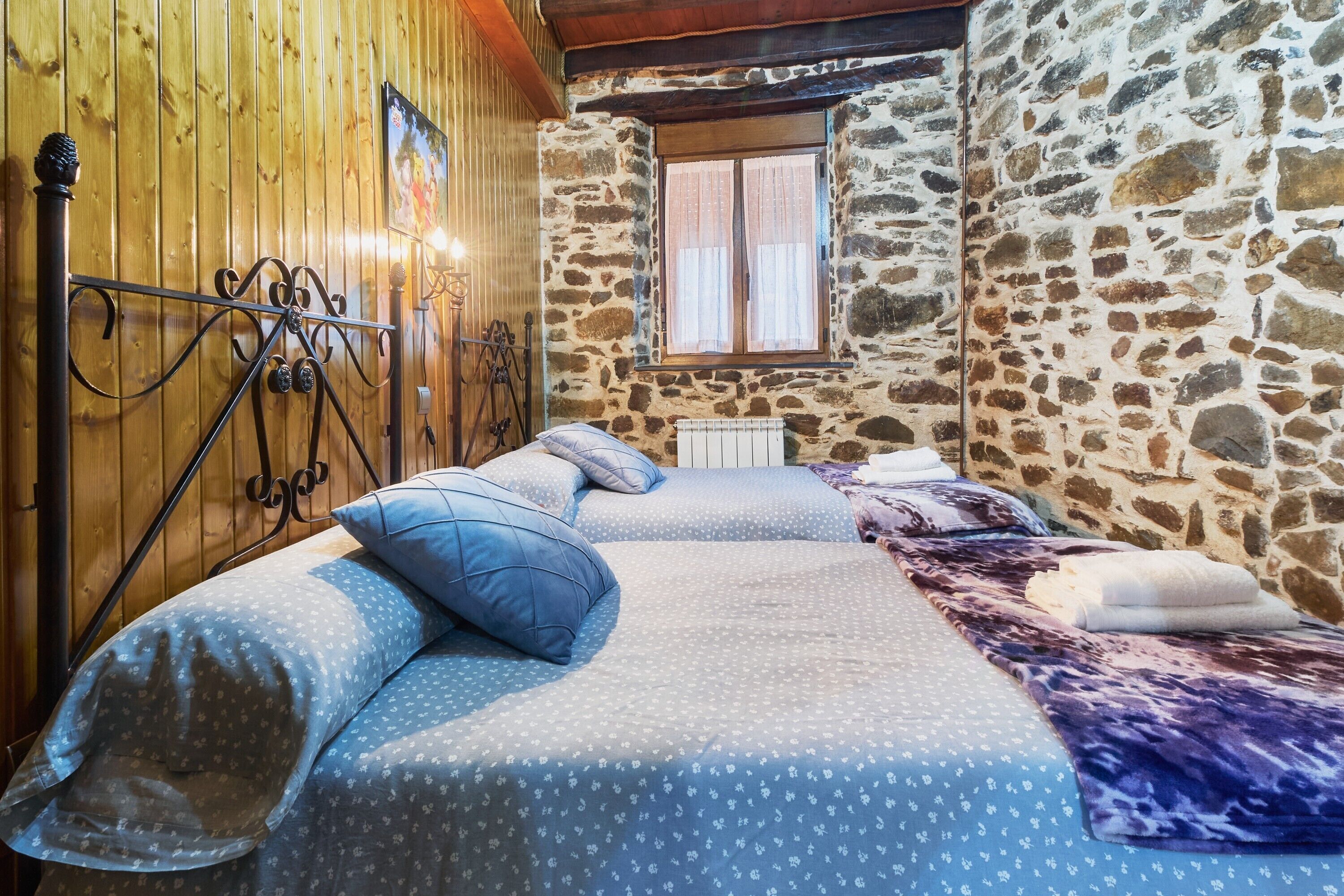 Een kamer met twee bedden, houten wanden, een stenen muur, een raam en een radiator.