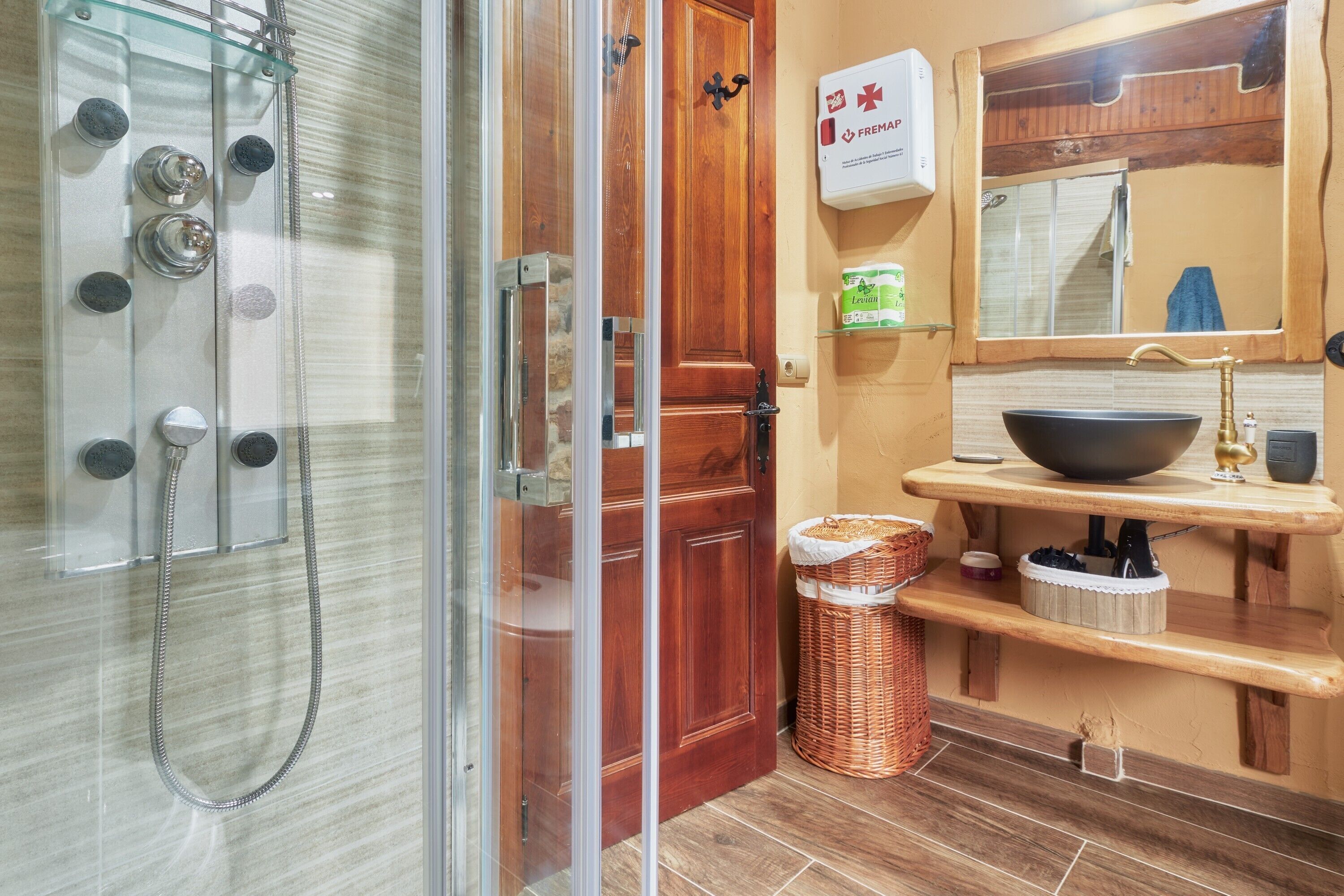 A bathroom with a glass-enclosed shower, a wooden door, a sink with a bowl, and a mirror above it.