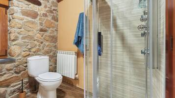 Une salle de bain avec un mur en pierre, des toilettes blanches, une douche en verre et une serviette bleue accrochée au mur.