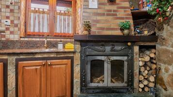 Una cocina con encimera de piedra, armarios de madera, chimenea con leña y una ventana con cortinas.