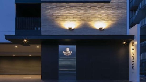A modern building facade with a textured surface and two illuminated signs. - Randor Hotel Sapporo Suites (Sapporo)