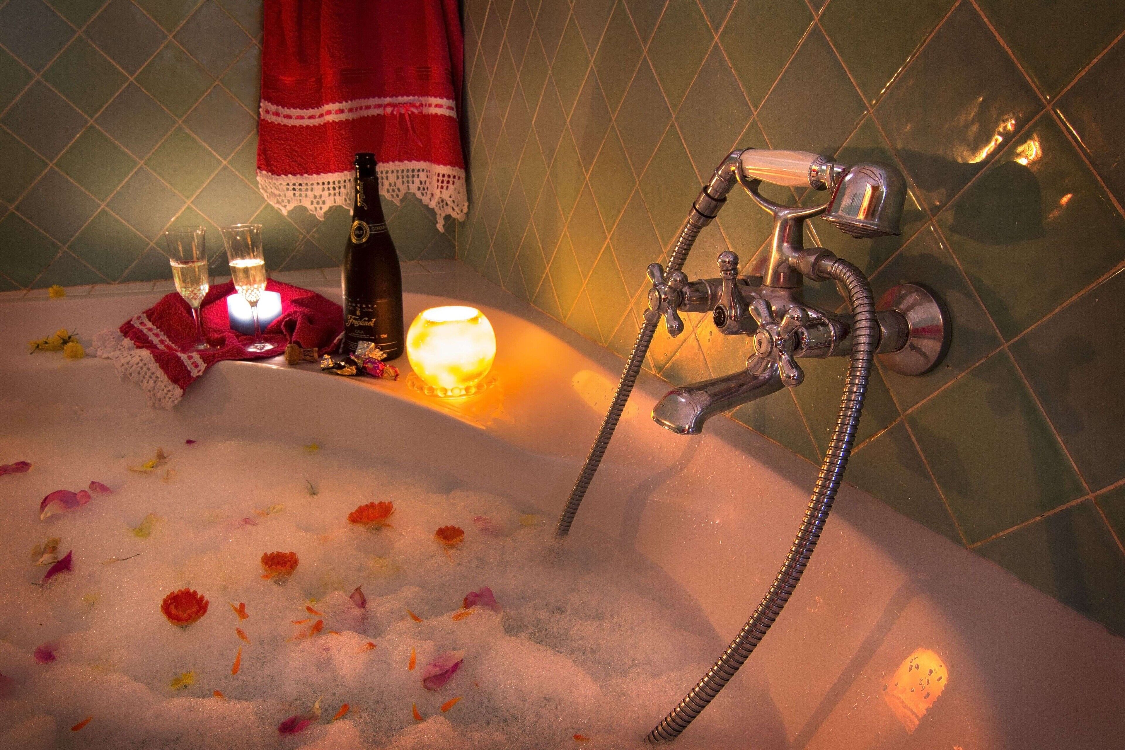 A bathtub with rose petals, a candle, and two glasses of wine.