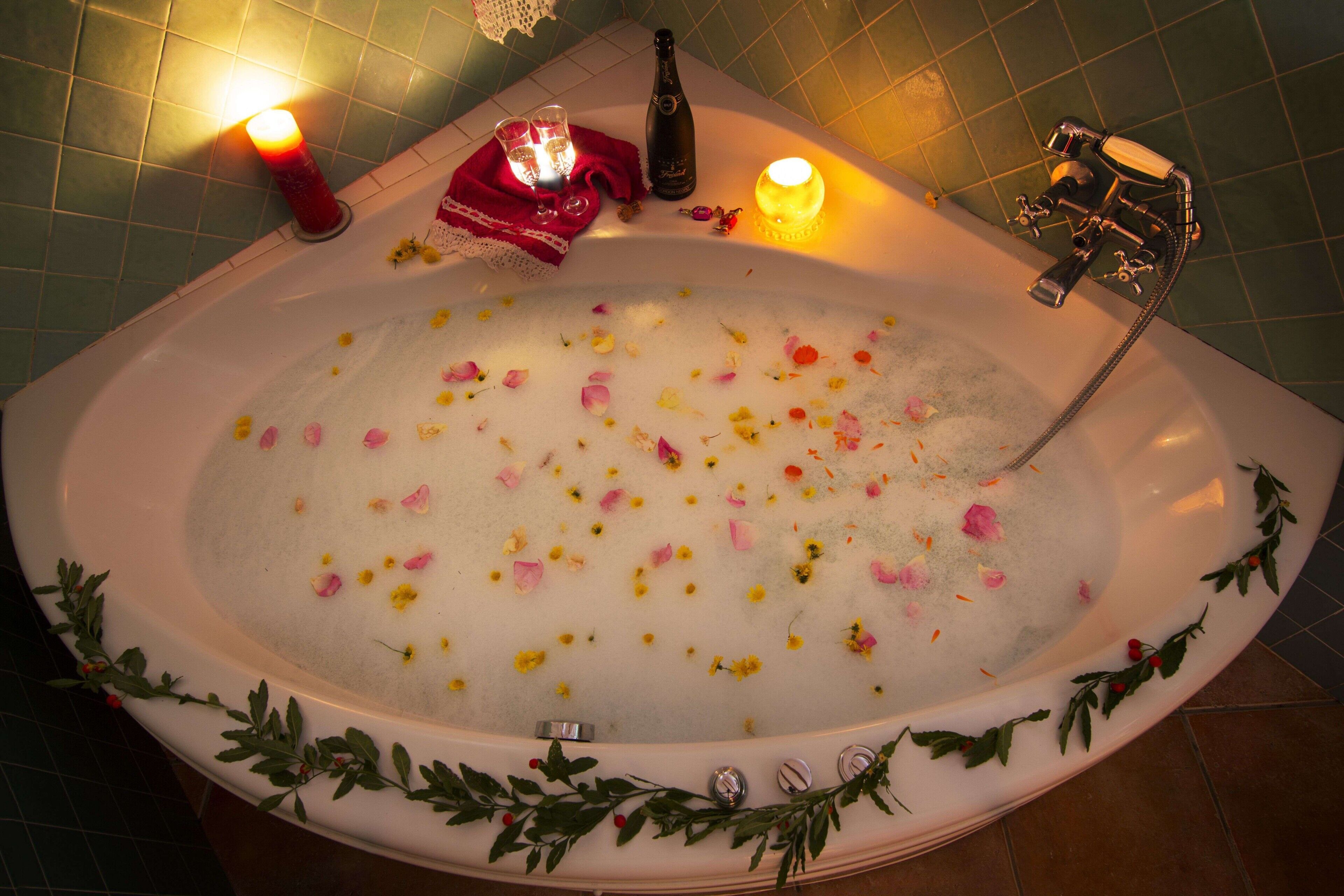 Una bañera con pétalos de rosa, velas y una botella.