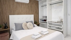 Camera da letto moderna con un letto grande, una parete rivestita in legno, un armadio bianco e un comodino con una lampada.