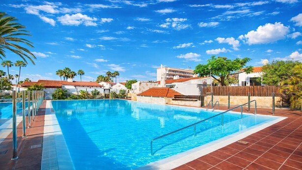 Una piscina con acqua cristallina, circondata da una terrazza piastrellata e palme.