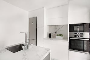 A modern kitchen with a marble countertop, stainless steel appliances, and white cabinetry.