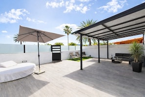 A rooftop patio with a covered seating area, a white wall, and a view of the sky.
