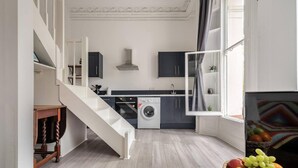 A modern kitchen with a built-in washing machine, a staircase, and a fruit basket on the floor. - West Oasis - Escape From Chaos (London)