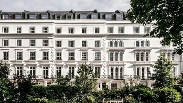 A large, multi-story building with a symmetrical facade, multiple windows, and a well-maintained lawn in the foreground. - West Oasis - Escape From Chaos (London)