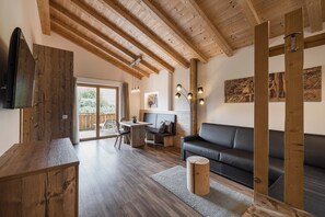 A modern living room with a wooden ceiling, a black leather sofa, a wooden table, and a TV mounted on the wall.