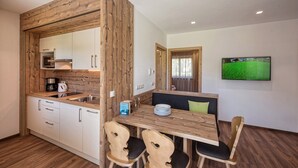 Una cocina moderna con detalles de madera, un comedor con mesa y sillas de madera, y un televisor montado en la pared.