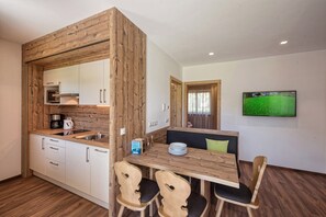 Eine moderne Küche mit Holzelementen, eine Essecke mit Holztisch und -stühlen sowie ein an der Wand befestigter Fernseher.