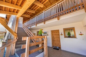 Een houten trap die naar een tweede verdieping leidt, met een balkon, een deur met de aanduiding '2' en een raam met een plant.