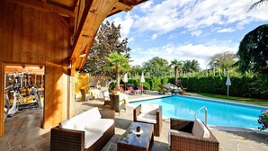 Un área de piscina al aire libre con mobiliario de mimbre, una zona de estar cubierta y equipo de ejercicio.
