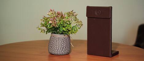 A round wooden table with a textured grey vase containing green plants and a brown leather wallet.