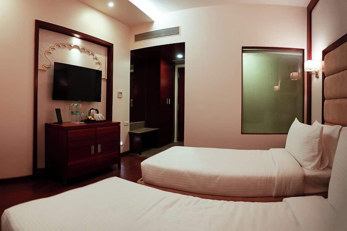 A hotel room with two beds, a TV, a desk, and a wardrobe.