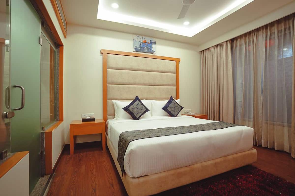 A hotel room with a large bed, a bedside table, a nightstand, a mirror, a window with curtains, and a ceiling light.