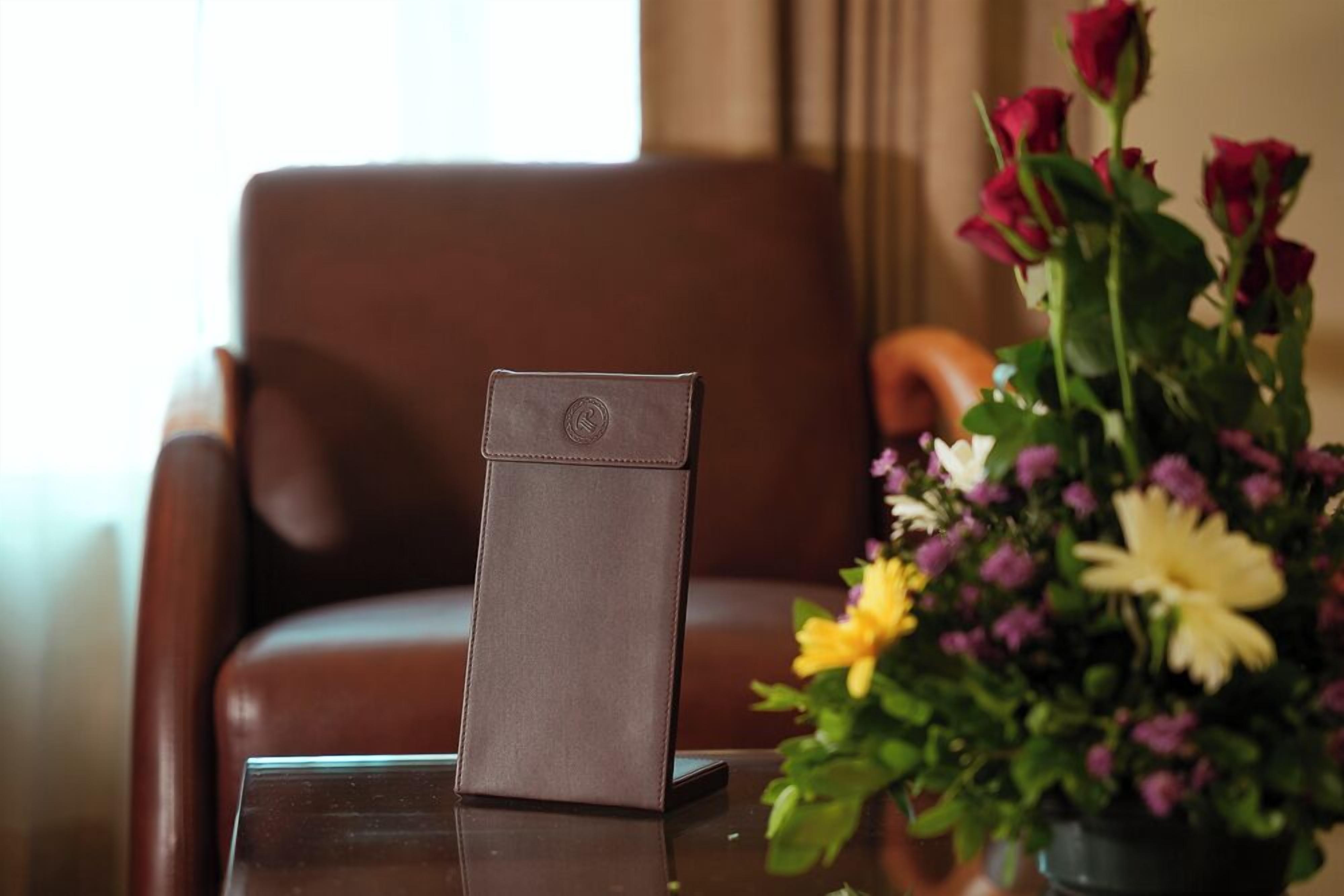 Una silla de cuero marrón con un teléfono inteligente en una funda de cuero sobre una mesa de vidrio.