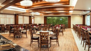 Un restaurant spacieux, doté de meubles en bois, d’un espace central pour le service et de grandes fenêtres offrant une vue sur la verdure.