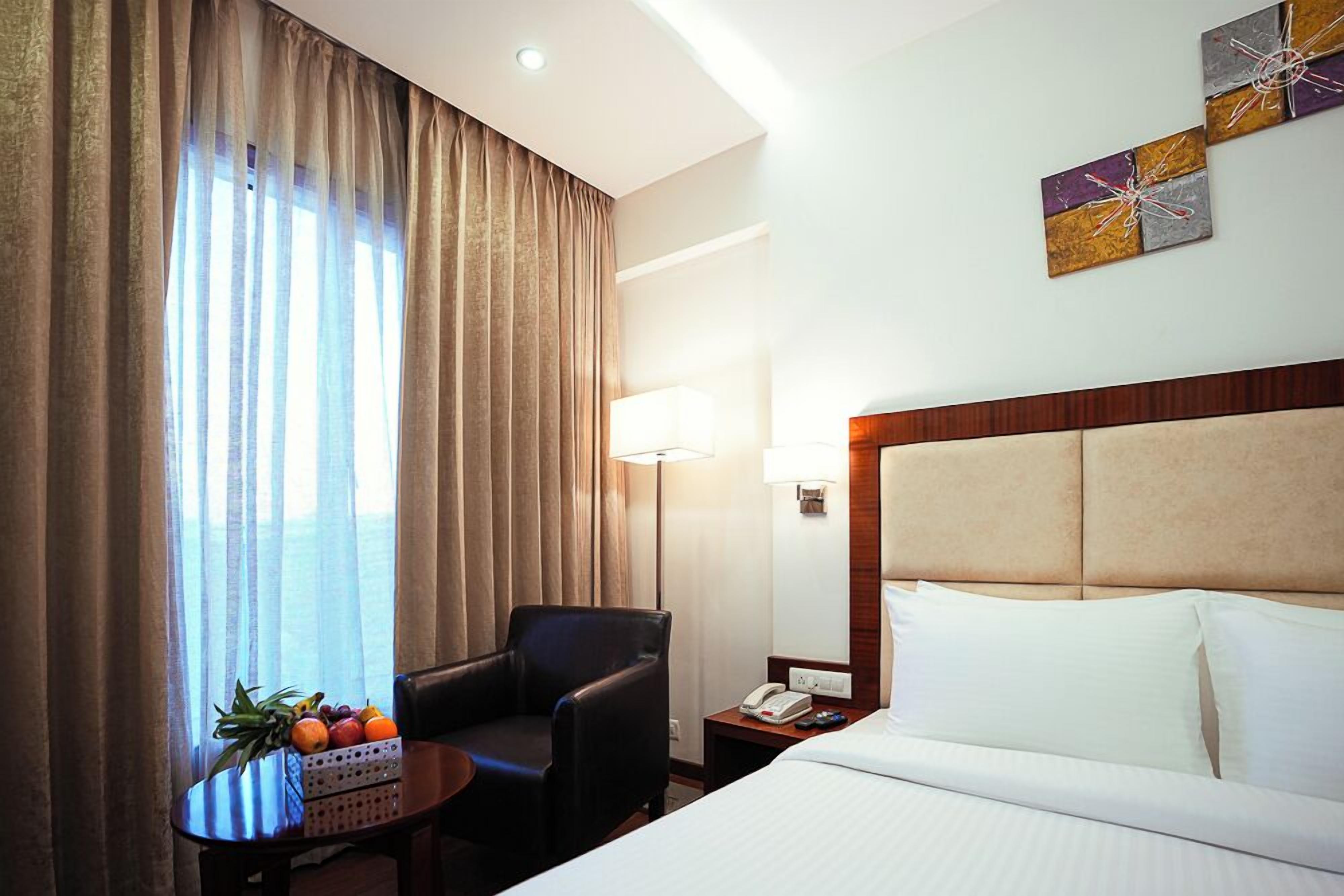 A hotel room with a bed, a desk with a lamp, a chair, and a fruit basket by the window.