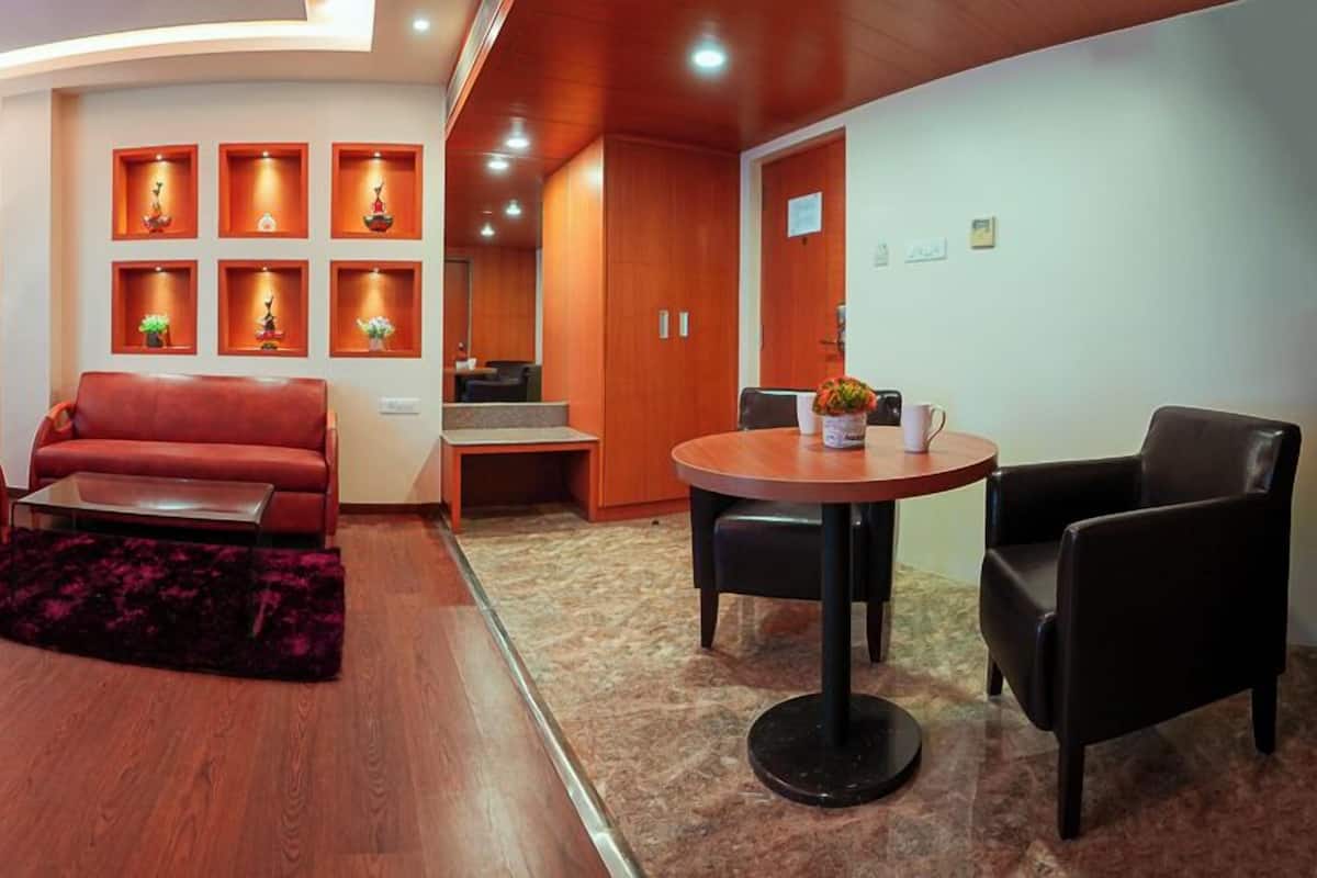 A modern living room with a red sofa, a coffee table, and a dining area with a round table and chairs. There are wall-mounted shelves with decorative items and a large window with curtains.