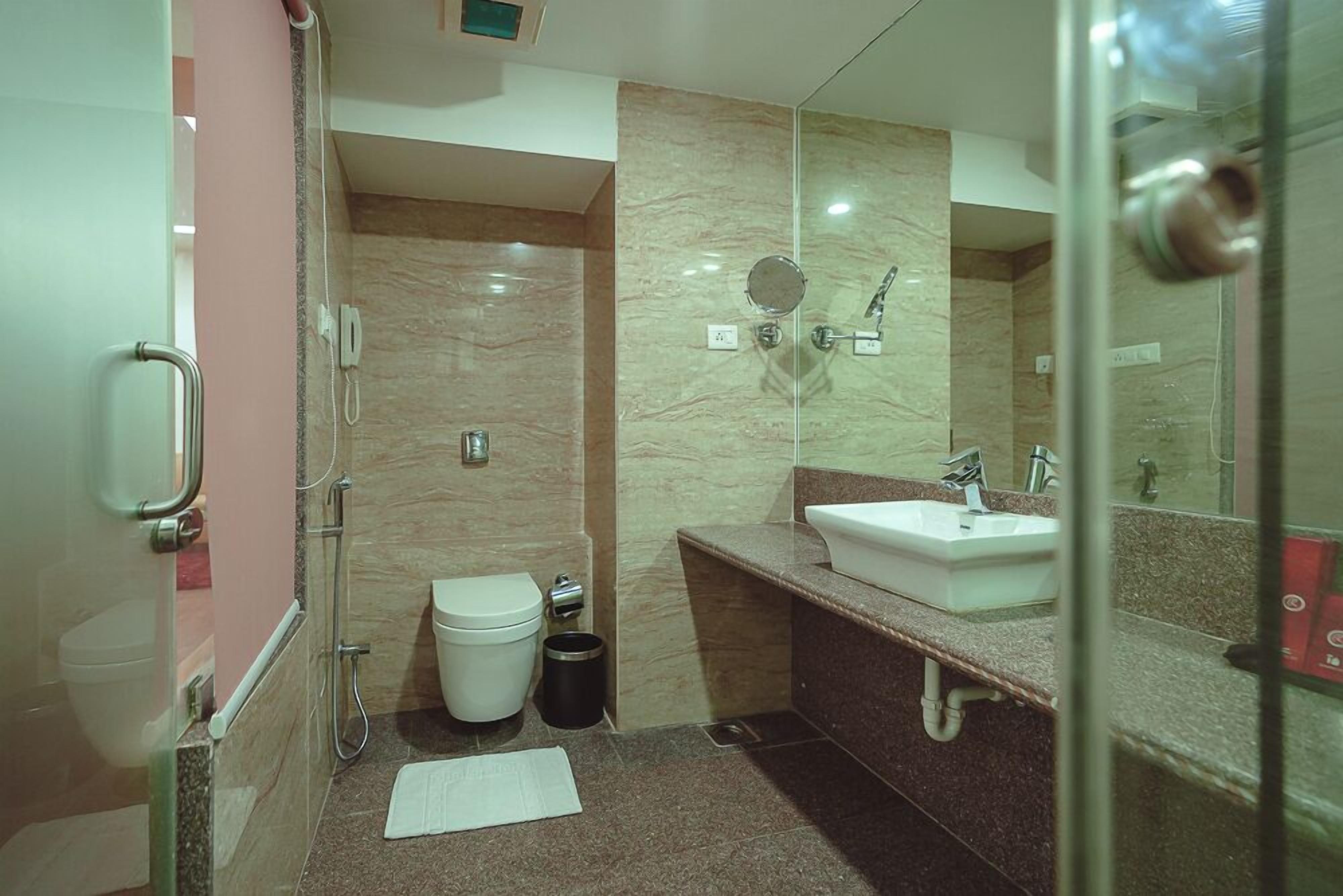A modern bathroom with a glass shower enclosure, a white toilet, a sink with a mirror, and a trash bin.