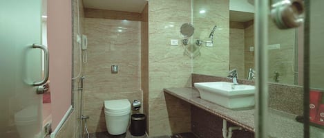 A modern bathroom with a glass shower enclosure, a white toilet, a sink with a mirror, and a trash bin.
