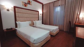 A hotel room with two beds, wooden flooring, a headboard, and a large window with curtains.