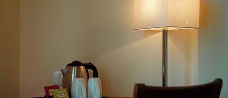 A hotel room with a desk, a tray with coffee cups and a kettle, and a lamp.