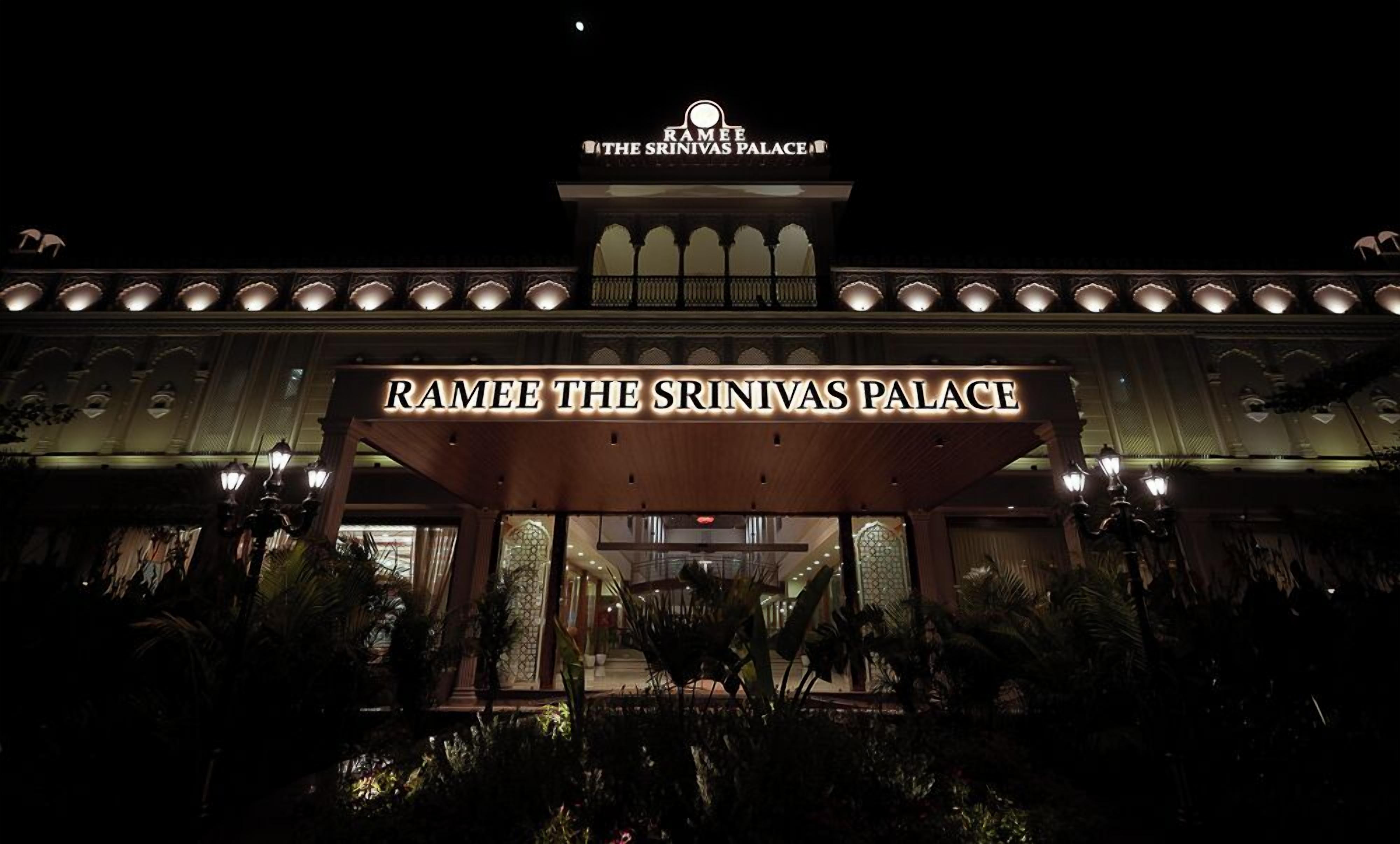 Exterior del Ramee The Srinivas Palace por la noche con señalización iluminada.