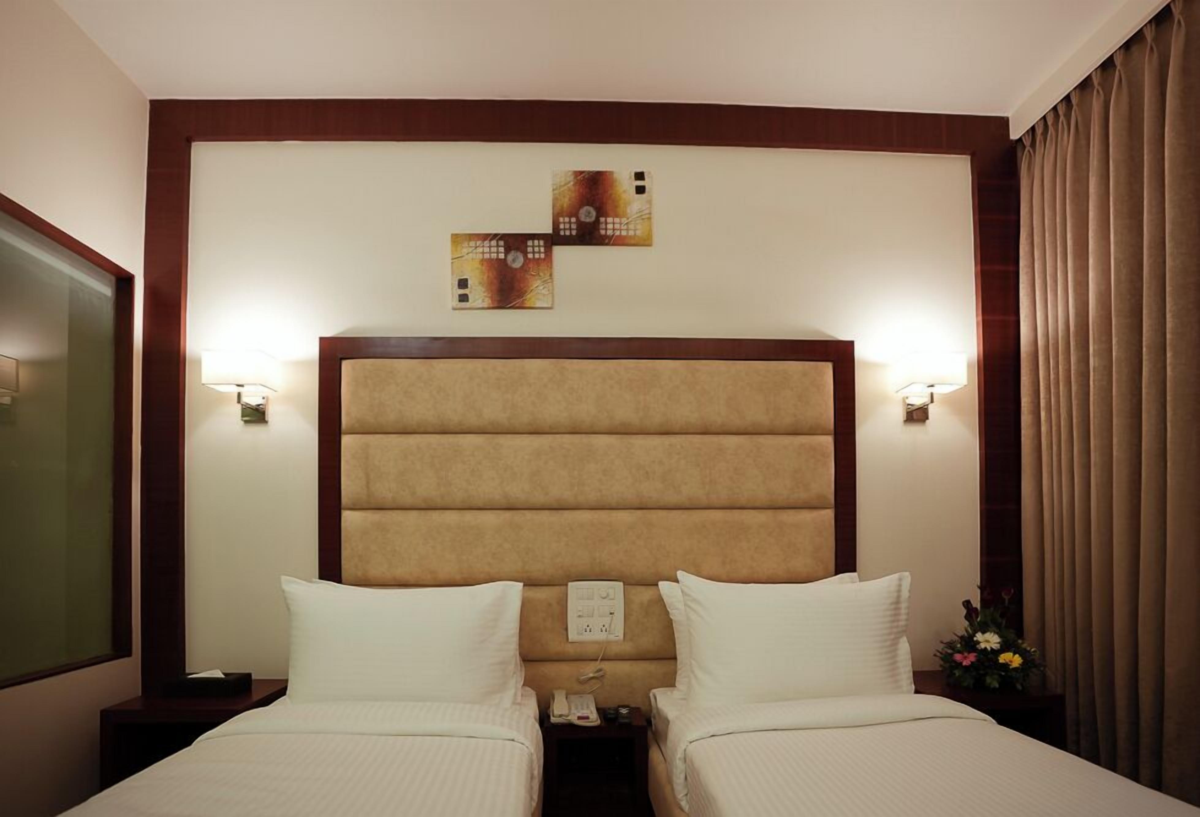 Habitación de hotel con dos camas, cabeceros, lámparas de noche, un teléfono y un adorno en la pared.
