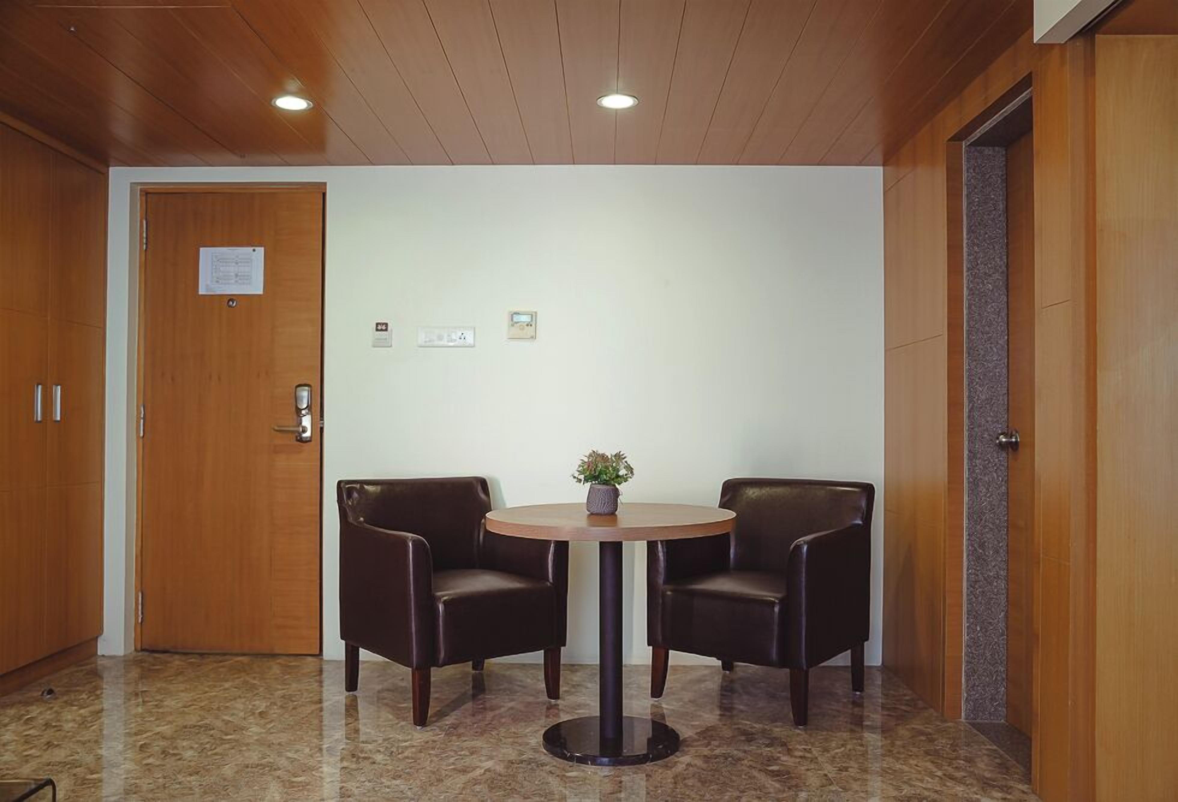 A lobby with a round table and two chairs, wooden doors, and a marble floor.